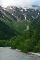 Obraz premium Mountain valley river forest snow cloud alpine landscape snow capped mountain valley with green forest and river under low cloud in remote alpine wilderness, natural travel scenery