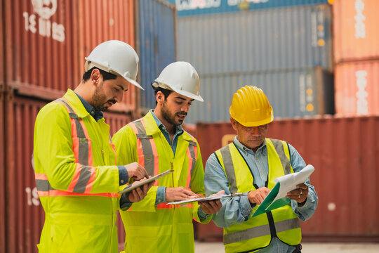 Worker hardhat safety vest clipboard container logistics shipping inspection port team review cargo document with serious expression at industrial container yard