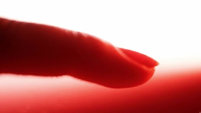 Close up of a human finger touching a smooth red surface, abstract macro shot with soft focus and bright white lighting