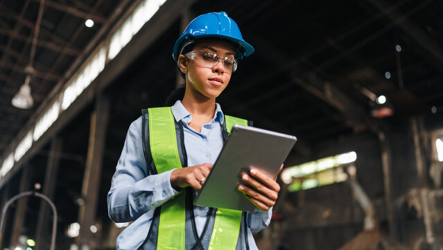 Engineer worker safety helmet tablet factory woman vest inspection focused female engineer using tablet in industrial factory, wearing safety gear during work
