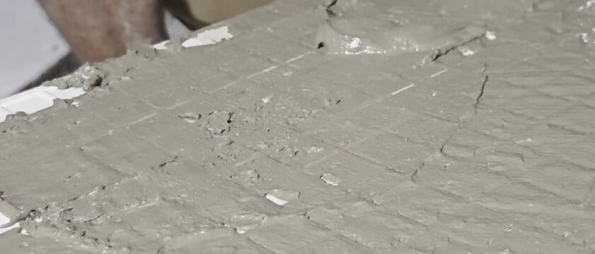 wet cement mortar slurry applied on floor with combed grid texture during tile installation. Target audience includes construction contractors, interior designers, architectural firms, building