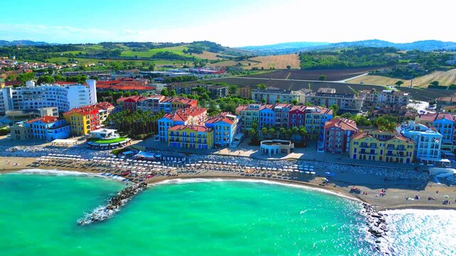 Premium aerial truck right pan left arcing shot of the Porto Recanati seaside, with the slightly wavy waters of the Adriatic Sea washing the shore with white foam, breakwaters, parasols, sandy beach
