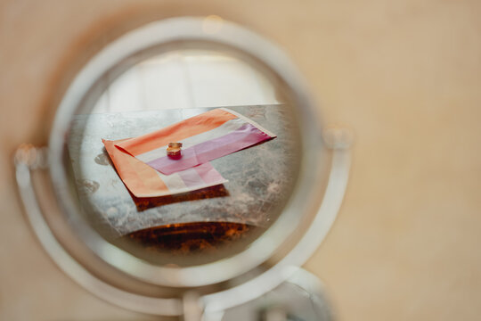 Creative composition of two wedding rings and a lesbian pride flag reflected in a small mirror, combining jewelry, rainbow colors and symbolism in a daytime setting.