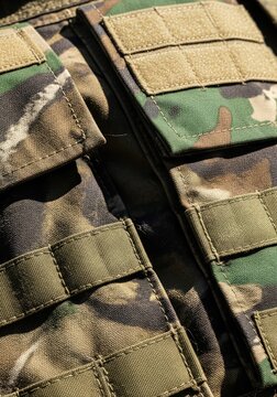 Close-up of a camouflage tactical vest with multiple pockets and straps, showcasing military-grade fabric and design details in natural light.