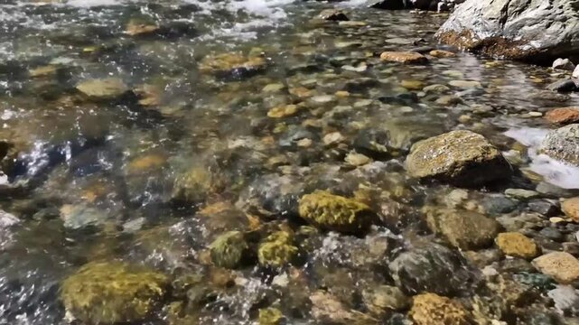 Close-up of a clear mountain stream with smooth and colorful rocks and pebbles flowing gently on a sunny day