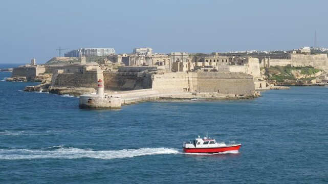 fort ricasoli grand harbour entrance valletta malta traditional maltese luzzu boat red pilot boat crossing lighthouse limestone bastion walls coastal fortification star fort headland defensive