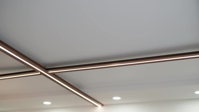 Slow-motion view of a modern ceiling with integrated LED strip and recessed spotlights, highlighting clean lines, minimalist architecture and warm contemporary interior lighting design