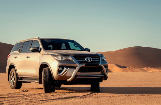 Gray Toyota Fortuner standing among the golden sands of the Namib Desert under a bright sky, capturing the spirit of off-road adventure, freedom, travel, and exploration in Namibia. 