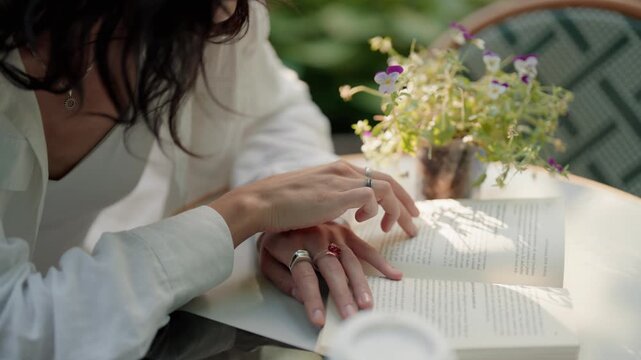 Romantic couple's hands interlacing and holding each other over an open book at a cafe terrace table, creating an intimate and peaceful moment together while enjoying a sunny day outdoors