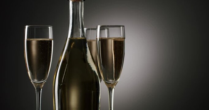 Elegant bottle of sparkling wine rotating with three glasses full of bubbling champagne on a dark, graduated background, symbolizing celebration, luxury, and a festive new year's eve party