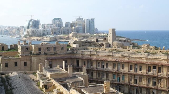 ruined fort barracks wing fort st elmo overlooking sliema skyline glass towers construction cranes mediterranean sea valletta malta coastal fortification abandoned military heritage architecture