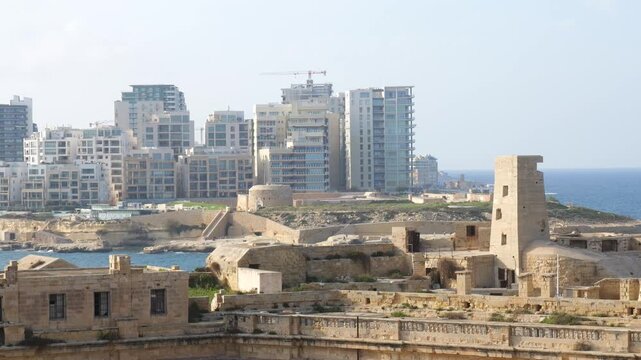abandoned barracks fort st elmo sliema skyline backdrop glass towers construction cranes mediterranean sea valletta malta coastal fortification ruins abandoned military heritage architecture