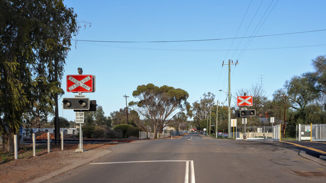 Rural level railroad crossing with flashing light signals and railway crossing crossbuck signs on an empty asphalt country road in an Australian town. Outback infrastructure
