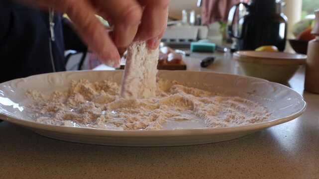 Hirtshals, Denmark A cook rolls white fish fillets in flour in a plate for frying in a pan. 