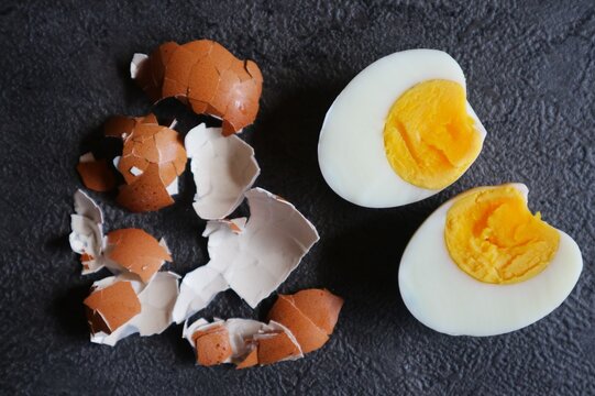 This photo shows a hard-boiled egg cut in half, surrounded by the brown eggshells that have been peeled off.