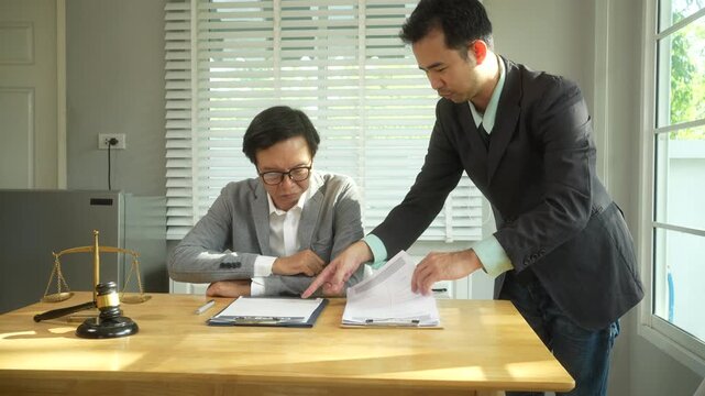 Lawyer reviewing documents with a client in a bright office while pointing at papers on the desk, with legal scales and a gavel nearby