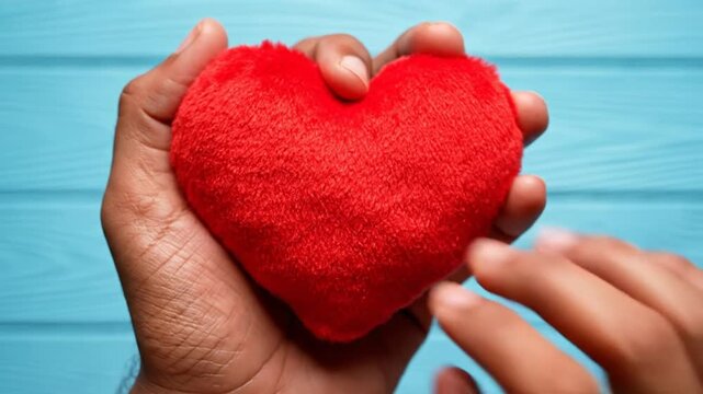 Hand cradling a red fluffy heart against a light blue wooden background with emotional love and care.