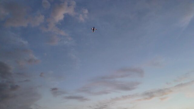 Wide angle stationary shot looking up at a commercial jet airliner cruising through a blue sky with scattered soft white and grey clouds during a serene sunset