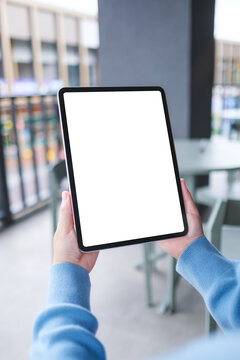 Vertical mockup image of a woman holding digital tablet with blank white desktop screen in cafe