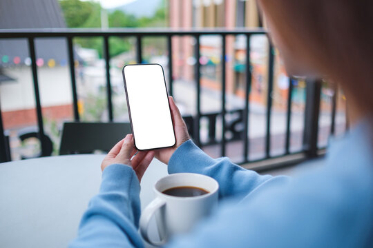 Mockup image of a woman holding and using mobile phone with blank desktop screen in cafe