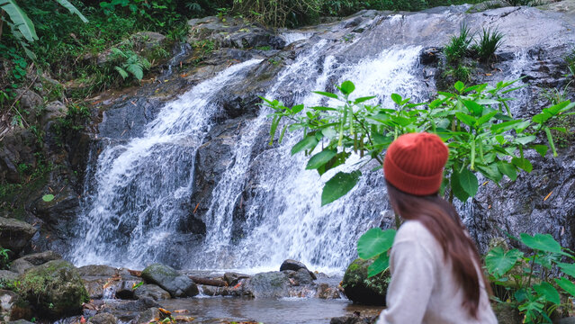 Rear view of a woman sitting and relaxing by the waterfall in the forest