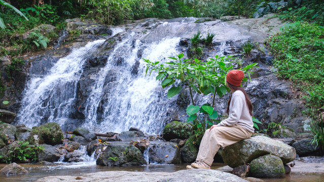 Rear view of a woman sitting and relaxing by the waterfall in the forest