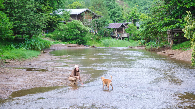 A woman playing with a dog by the river in rural village