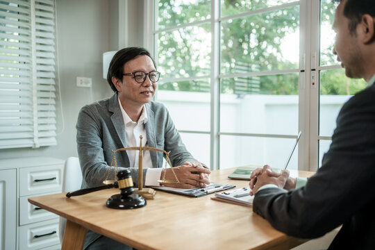Two men meeting in a bright office with legal scales, gavel, and documents on a desk, discussing a case or business matter