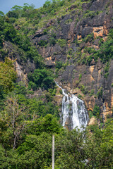 Waterfall cascades down rugged rocky cliffs surrounded by lush green forest in the highlands of Nuwara Eliya, Sri Lanka © nilanka