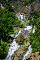 Waterfall cascades down rugged rocky cliffs surrounded by lush green forest in the highlands of Nuwara Eliya, Sri Lanka © nilanka