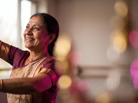 Portrait of happy mature Indian woman in traditional saree dancing in sunlit room