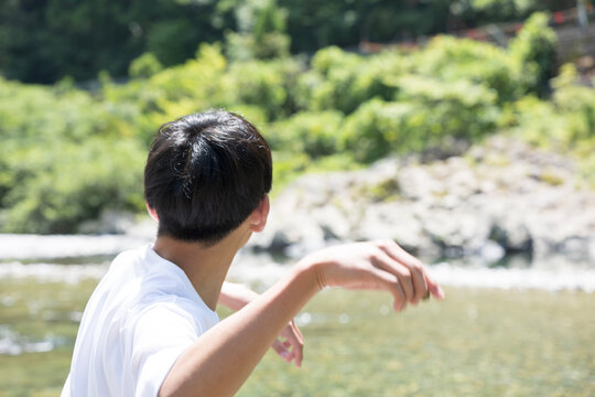 自然の中で水遊びを楽しむ夏のレジャーやお出かけの少年時代のイメージ　石切りをする少年の顔なしの後姿