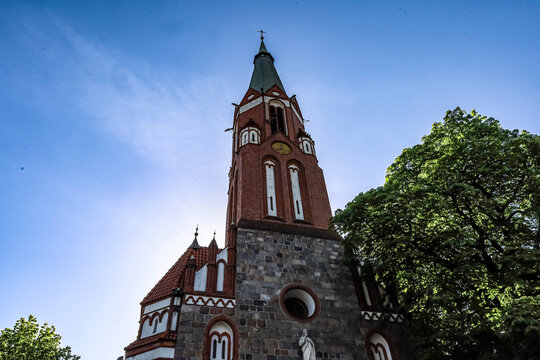 Historic red brick church tower with a green spire against a bright blue sky