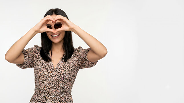 Young woman making heart shape with hands smiling on white background