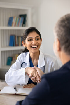 Smiling South Asian female gp or nurse shaking hands with male patient during consultation, representing trust, agreement on treatment and positive doctor patient relationship after health checkup