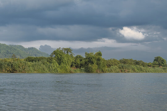 Dramatic storm clouds gathering over Dong Nai River in Cat Tien National Park, Vietnam. Panoramic landscape of lush green tropical forest bank under dark cloudy skies before rain.