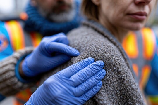 Paramedic hands securing blanket around woman's shoulders outdoors