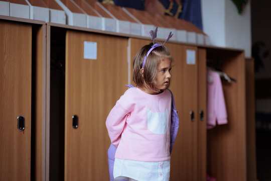 Girl Taking Off Jacket Inside Kindergarten Cloakroom in the Morning. Kid removes her warm winter clothing at preschool locker room