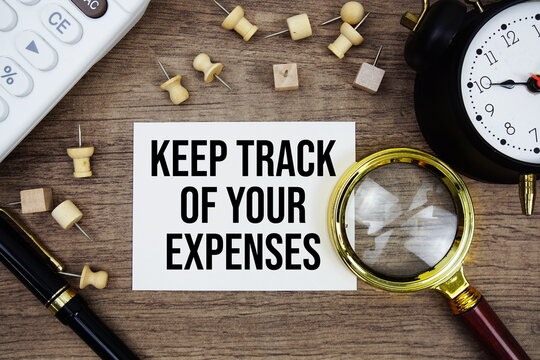 Keep Track Of Your Expenses text written on notepad with pen, alarm clock, magnifying glass and calculator on wooden background