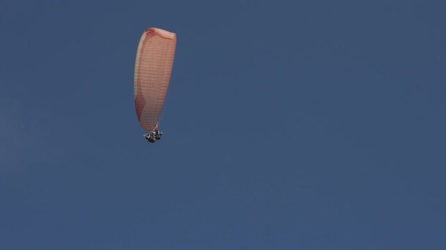 Paraglider glides high above green hillside. Clear blue sky frames aerial adventure. Soaring person enjoys freedom above nature. Perfect for travel, sport, or outdoor activity themes
