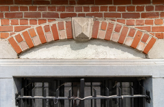 Architectural detail of a brick arch window with stone keystone and metal security grille