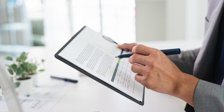 Close up of hands with pen of young businessman  at desk review document papers , analyzing information.