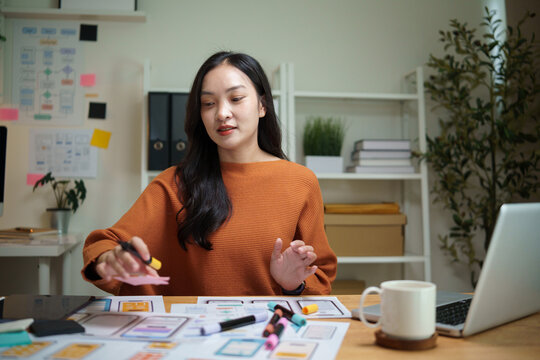 Female UX designer working on mobile app wireframes and interface layouts with colorful markers at a creative office desk.