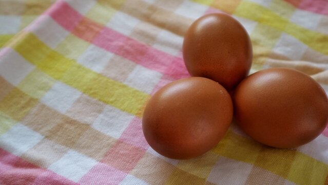 Three brown eggs on pastel checkered cloth with copy space