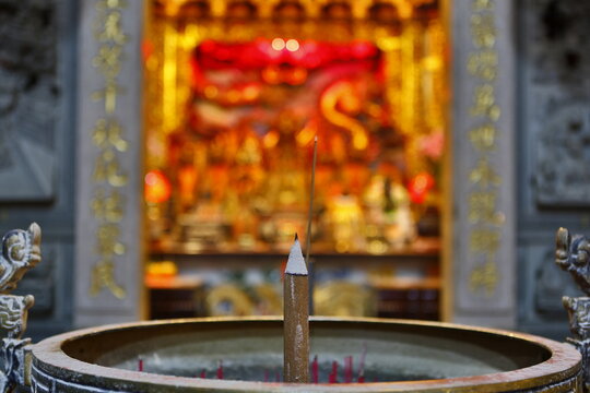 A burning incense stick stands in a temple burner.