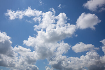 Obraz premium Bright Blue Summer Sky with Fluffy White Clouds. Expansive view of a bright blue summer sky filled with beautifully shaped white cumulus clouds. The natural cloudscape has a cheerful, airy atmosphere 