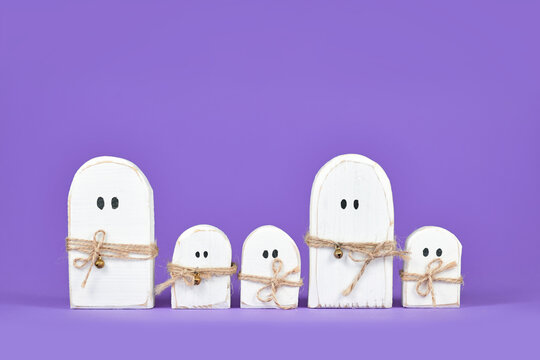 Cute wooden Halloween ghost ornaments in a row on purple background