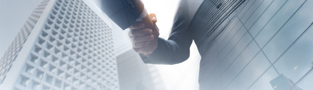 Businessman hand shaking with partner, low angle view with modern business buildings background, Business cooperation, Investment and finance, Successful deal
