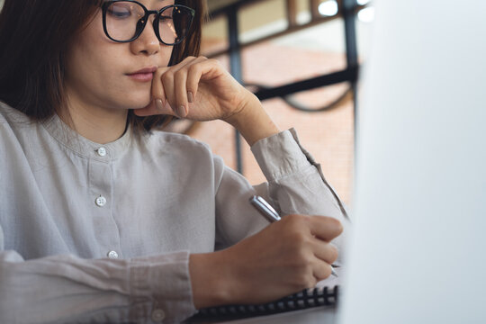 Close-up of thoughtful businesswoman writing notes using laptop, working remotely in office modern workspace, focused productivity concept.