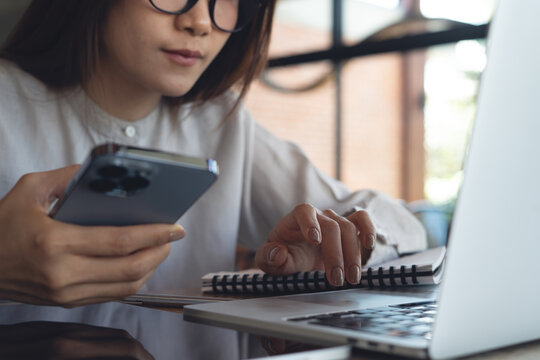Focused woman working on laptop, browsing the internet and using smartphone at modern office, close up. Remote work,  online business lifestyle concept.